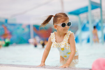 Cute child in a hat and glasses swims and plays in the pool on vacation at the water park