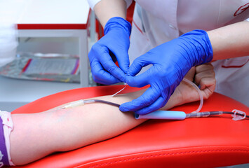 Nurse hands in blue gloves taking blood from vain of donor with hypodermic needle