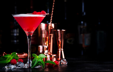 Summer red  cocktail with gin, raspberry syrup, lime juice, quail egg white and ice in glass. Black bar counter background