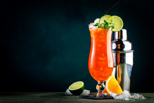 Summer alcoholic cocktail drink with dark and white rum, ice, pineapple, orange juice, lime and ice, with mint. Dark background, bar tools