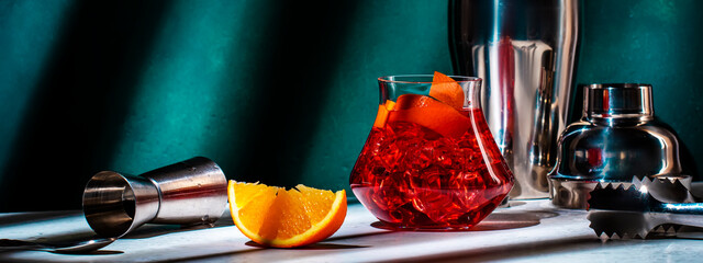 Strong red alcoholic cocktail drink with bourbon, vermouth, bitter, orange zest and ice. Dark green...