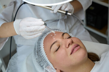 Professional cosmetologist performing electrical facial treatment on woman