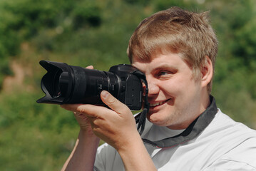 dslr camera in hands, young adult caucasian photographer in white t-shirt at work outdoors in sunny summer day, looking left and taking picture