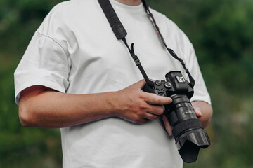 dslr camera in hands, young adult caucasian photographer in white t-shirt at work outdoors in sunny summer day