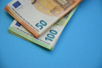 Many banknotes of 100 and 50 Euro bills on light blue paper background