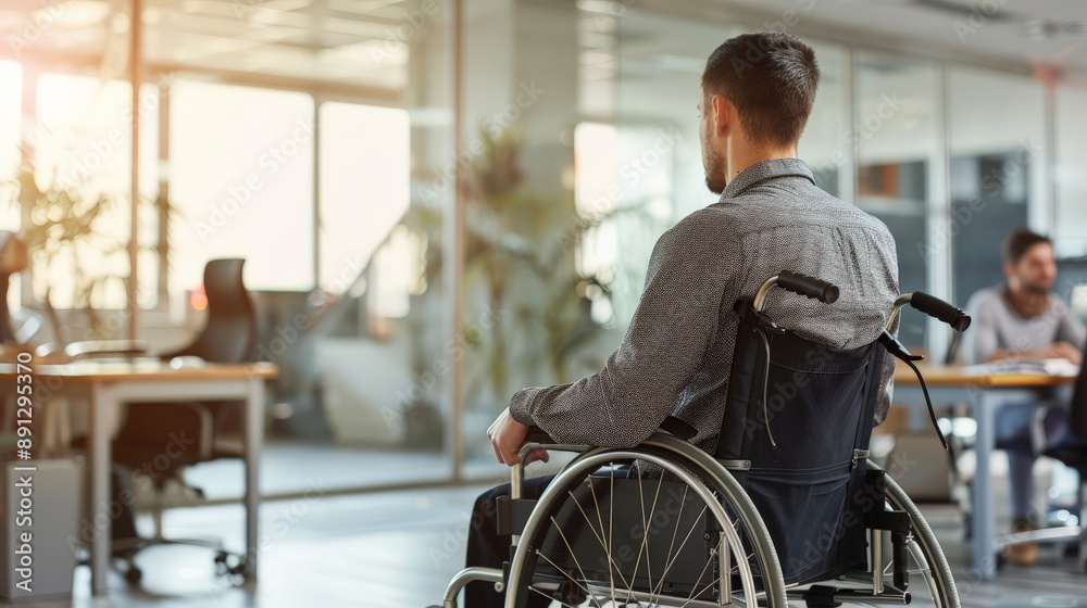 Poster man in a wheelchair facing away, working in a bright open office. emphasizing accessibility and empl