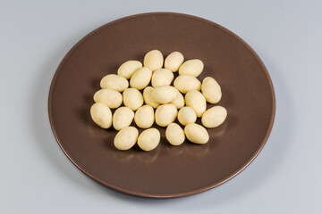 Almonds covered with white chocolate on dish on gray background