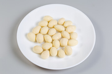 Almonds covered with white chocolate on dish on gray background