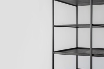 Empty black metal shelving unit standing near white wall
