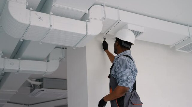 African worker install ducted pipe system for ventilation and air conditioning in office