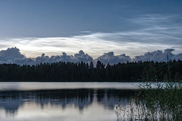 charming night landscape with silver clouds, silver clouds over the lake, dark forest silhouette in the background, mesospheric clouds