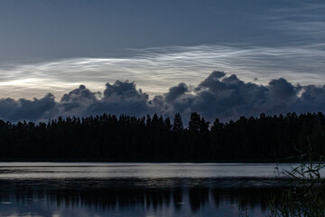 charming night landscape with silver clouds, silver clouds over the lake, dark forest silhouette in the background, mesospheric clouds