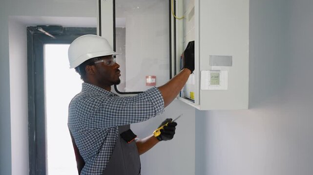 African american male electrician works in a switchboard with an electrical connecting cable