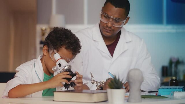 African American boy and father in lab coats examining samples under microscope
