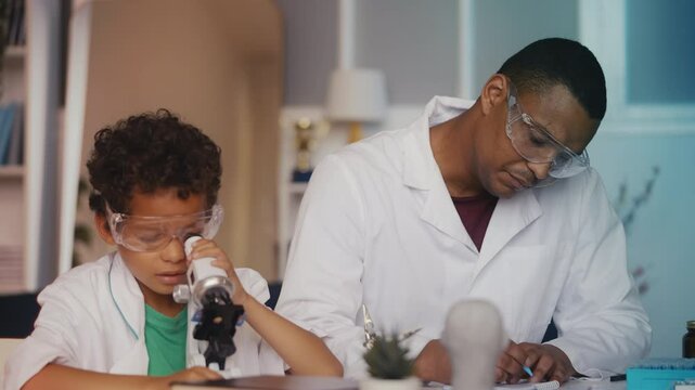 Little boy and his dad playing scientists, looking at samples under microscope
