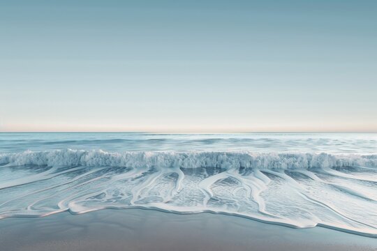 A peaceful scene capturing ocean waves gently washing onto the sandy beach under a light blue sky. The calm tide and serene ambiance evoke relaxation and tranquility.