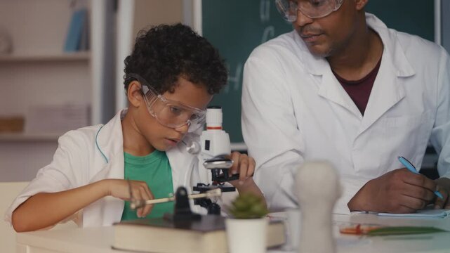 Boy in lab coat places sample under microscope, dad documents test results