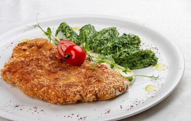 Chicken schnitzel served with sauce, accompanied by broccoli and cheese fritters.