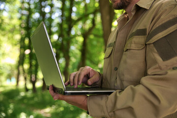 Forester with laptop examining plants in forest, closeup
