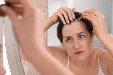 Naklejka premium Hair loss problem. Woman applying serum onto hairline near mirror indoors