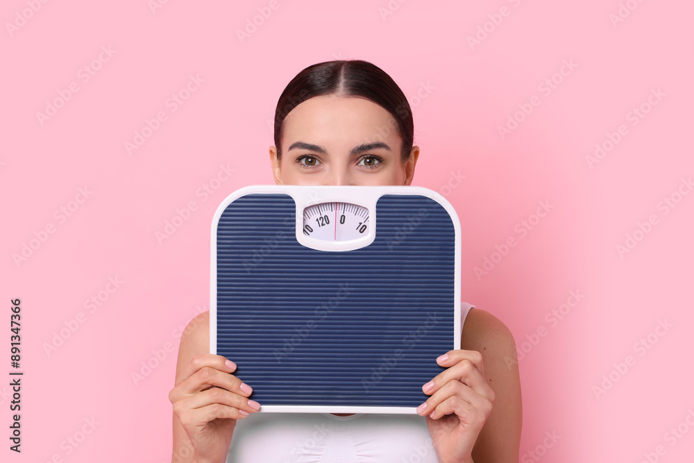 Poster Diet and weight loss concept. Young woman with floor scale on pink background