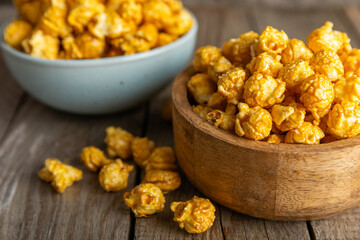 Sweet caramel popcorn in a bowl on a wooden background. Salted caramel popcorn. Caramel sauce. Close up. Topping. Place for text. Copy space