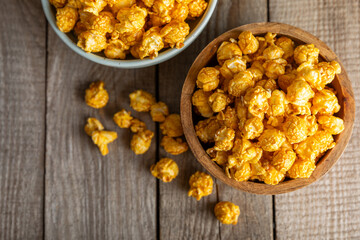 Sweet caramel popcorn in a bowl on a wooden background. Salted caramel popcorn. Caramel sauce. Close up. Topping. Place for text. Copy space