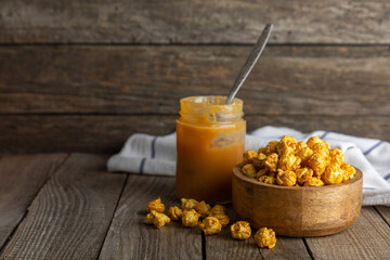 Sweet caramel popcorn in a bowl on a wooden background. Salted caramel popcorn. Caramel sauce. Close up. Topping. Place for text. Copy space