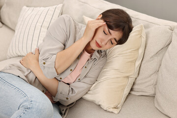 Upset woman suffering from headache on sofa at home