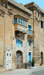 A historic stone building featuring vibrant blue doors and windows, showcasing traditional architecture and urban heritage on a sunny day.