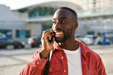 Happy young African Black man hipster or tourist with backpack standing on city street outdoors...