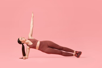 Young woman doing aerobic exercise on pink background