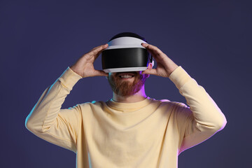 Smiling man using virtual reality headset on dark purple background