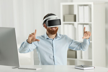 Smiling man using virtual reality headset at workplace in office
