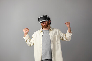 Emotional man using virtual reality headset on grey background