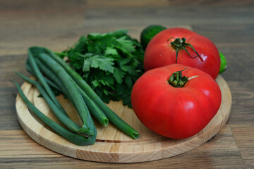 a cutting board with a bunch of green vegetables and red tomatoes on it 