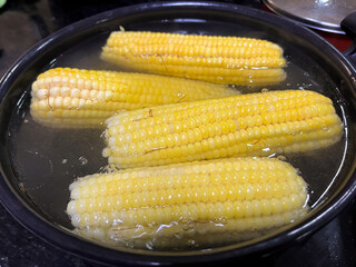 Four ears of corn being boiled in a pot.