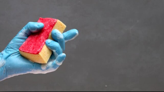 Hand in blue rubber glove squeezes red washing sponge and shows thumb up with soapy foam for cleaning and washing design