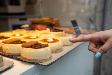 Hand pointing at desserts in a shop window. Hand with blue nails pointing at various desserts displayed in a shop window