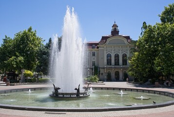 Fototapeta premium Plovdiv, Bulgaria - Jun 30, 2024: Plovdiv city hall. People walking in Ancient Philippopolis on sunday. Streets and buildings. Lifestyle in the urban area. Sunny summer day. Selective focus