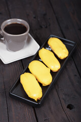Yellow Glazed Eclairs and Black Coffee on Dark Wood Background - Perfect Pairing for a Cozy Afternoon Coffee Break