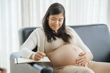 A pregnant mother sits on the sofa, looking at her phone and shopping online. She is preparing to...