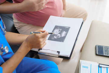 Fototapeta premium Pregnant mothers meet the nurse at the clinic as scheduled, reviewing their medical history and discussing symptoms. Sitting on the sofa, they report headaches, nausea, and back pain to the nurse.