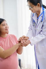 Fototapeta premium A pregnant woman sits on the sofa in the clinic. The doctor examines her abdomen and reviews the ultrasound results. Offering encouragement, the doctor holds her hand, providing support and care.