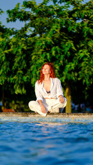 A beautiful young red-haired woman spends time in a park by the pool