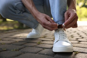 Man tying shoelace of white sneaker outdoors, closeup