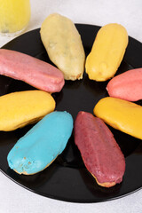 A close-up of colorful &eacute;clairs perfect for food blogs, recipe websites, and social media. The &eacute;clairs are arranged in a circular pattern on a black plate, creating a visually appealing image.