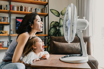 Mother and daughter refreshing at home with electric fan during
