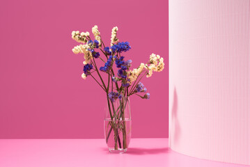 Ramo de flores secas azules y amarillas en un jarrón con agua sobre un fondo rosa