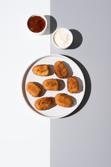 Plato de croquetas fritas con salsa de tomate y mayonesa aperitivo sobre mesa blanca y gris. Vista superior